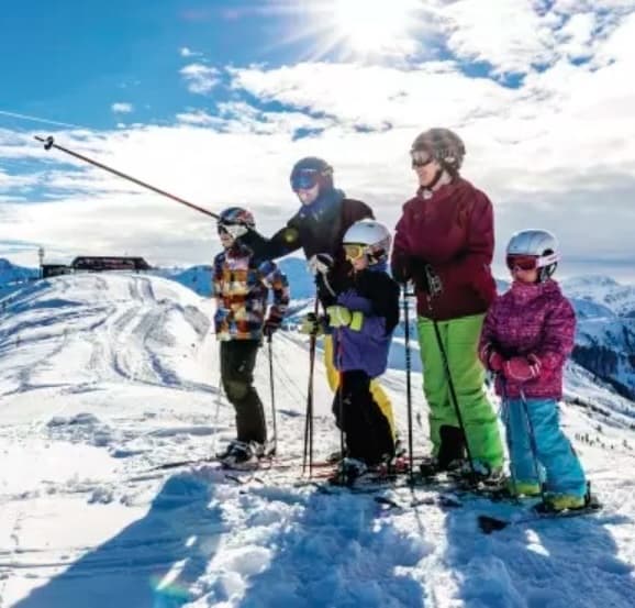 A family of five in ski gear standing together on a sunny mountain ridge